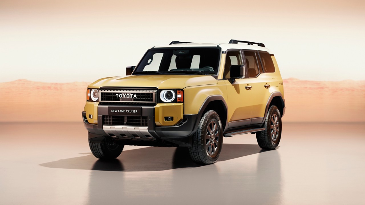 A front view of the all-new Toyota Land Cruiser parked at an angle. Its bright metallic gold paint contrasts with the orange studio setting.